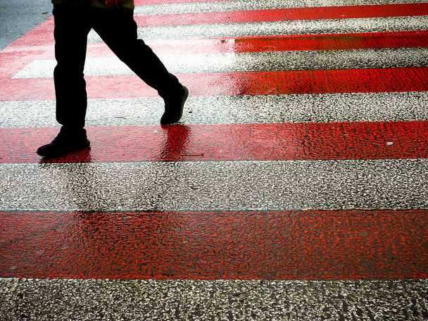 Male figure walking on red and white zebra crossing. - Photo, Image