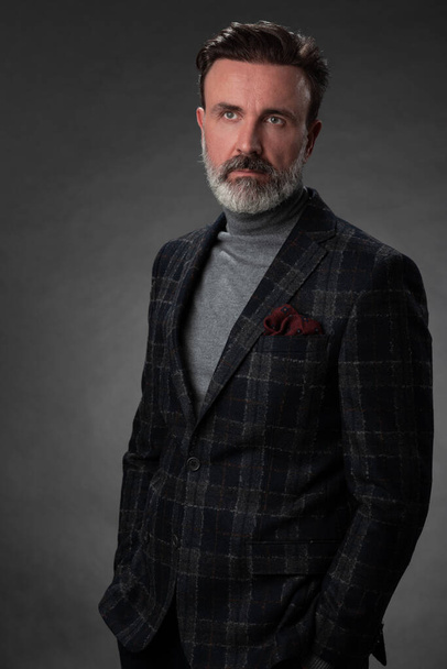 Portrait of a stylish elegant senior businessman with a beard and casual business clothes in photo studio isolated on dark background gesturing with hands - Photo, image