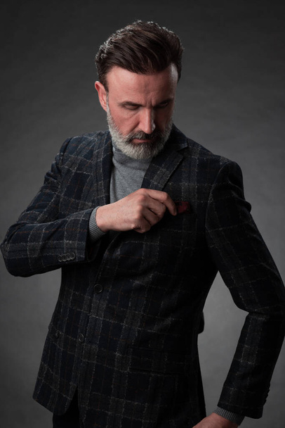 Portrait of a stylish elegant senior businessman with a beard and casual business clothes in photo studio adjusting suit - Photo, image