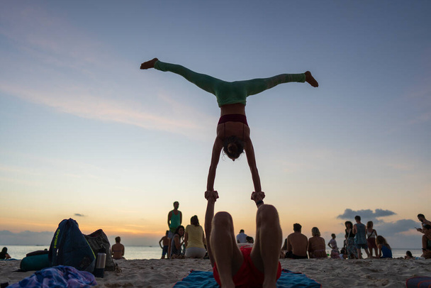 Koh Phangan, Thailand - Jan, 23, 2022 : Young man and woman exercising acro yoga on the beach near the sea during sunset on the tropical island of Koh Phangan, Thailand. Close up - Zdjęcie, obraz