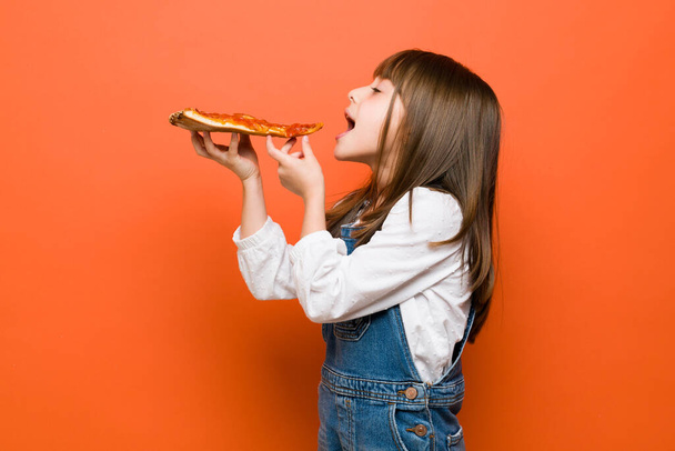 プロフィールビューの小さなブルネットの女の子の服装カジュアルと噛もうとしていくつかのピザでスタジオ - 写真・画像