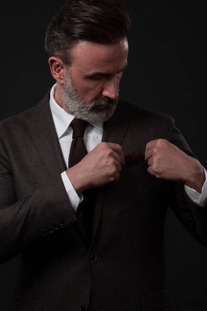 Portrait of a stylish elegant senior businessman with a beard and casual business clothes in photo studio adjusting suit - 写真・画像