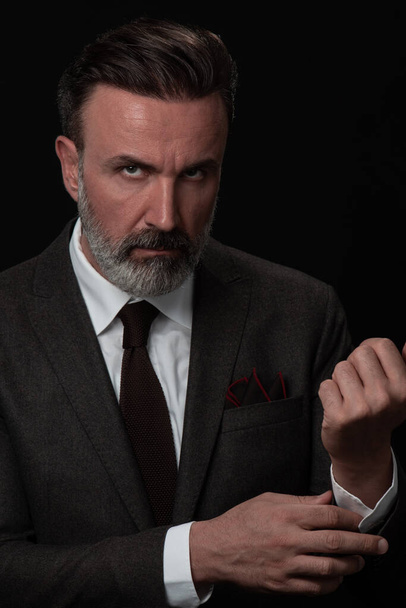Portrait of a stylish elegant senior businessman with a beard and casual business clothes in photo studio adjusting suit - Фото, зображення