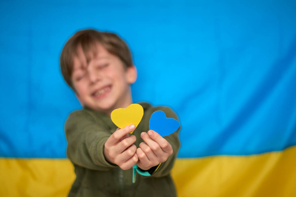 Ragazzo mani in possesso di cuori di carta giallo-blu su sfondo bandiera ucraina. I bambini sostengono l'Ucraina, fermare la guerra, rimanere con l'Ucraina hashtag - Foto, immagini