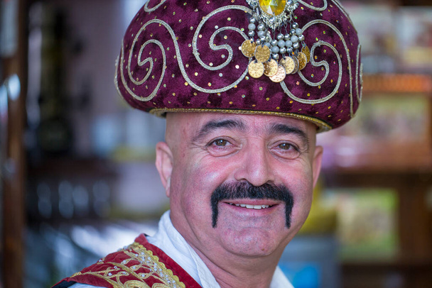 Kemer, Turkey - Oct 18, 2017 : Portrait of a Turkish man dressed in national clothes, which sells oriental sweets at a local street market in Kemer, Turkey . Close up - 写真・画像
