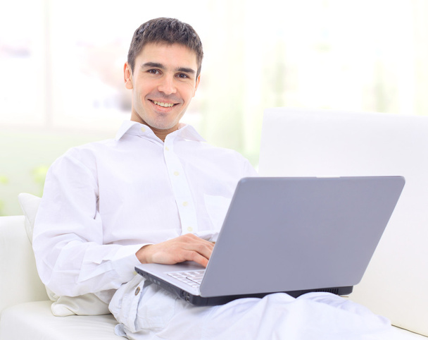 Happy young man sitting on sofa with a laptop - Zdjęcie, obraz