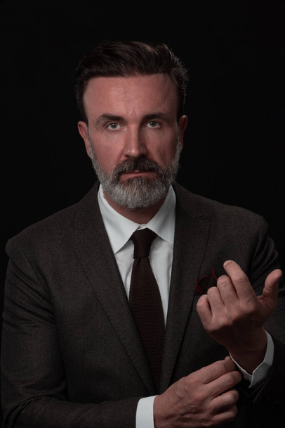Portrait of a stylish elegant senior businessman with a beard and casual business clothes in photo studio adjusting suit - Fotó, kép