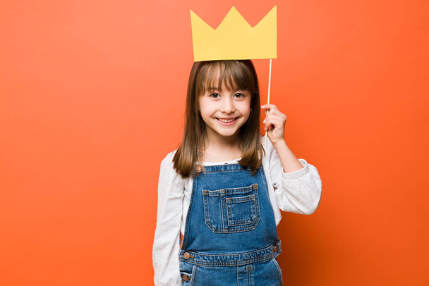 Ritratto di una graziosa bambina bruna con una corona di carta sulla testa che gioca a fare la principessa con un sorriso - Foto, immagini