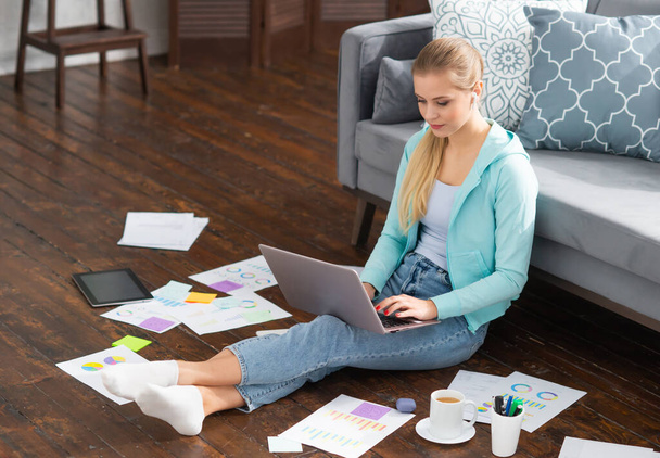 Young woman works with documents using a laptop while sitting on the floor at home. Student, entrepreneur or freelancer girl working or studying remotely via internet. - Photo, image