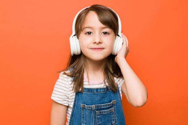Portret pięknej dziewczynki noszącej słuchawki bezprzewodowe i nawiązującej kontakt wzrokowy podczas słuchania muzyki - Zdjęcie, obraz