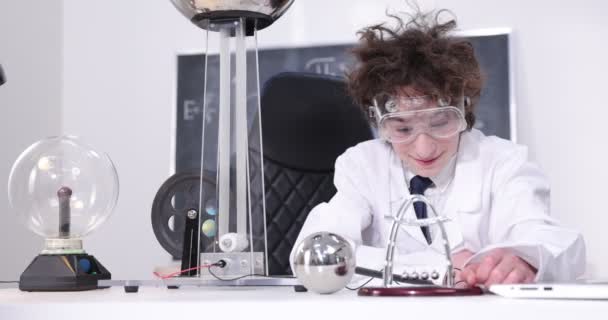 Koulutus, tiede ja lapset käsite poika yllään suojalasit fysiikan lab tekee sähkötestejä. Lapsi opiskelee sähköpurkauksia laboratoriossa. - Materiaali, video
