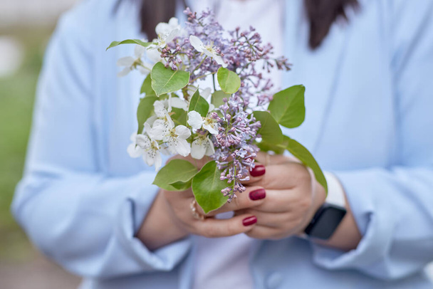 Estetické jarní květiny v ženských rukou se uzavírají. Lilac a meruňka kvetou. Jarní pozadí.  - Fotografie, Obrázek