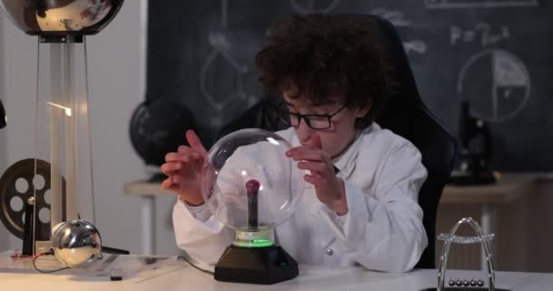 Fysiikan laboratorio: komea nuori tiedemies valkoisessa takissa ja laseissa tekemässä sähkötestejä. Lapsi opiskelee sähköpurkauksia laboratoriossa. - Materiaali, video