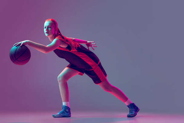 Portrait of young girl, teen, basketball player in motion isolated over gradient pink purple background in neon. Professional player - Fotoğraf, Görsel