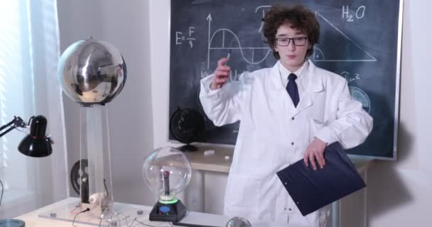 物理学研究室:白衣と眼鏡を着たハンサムな若い科学者が電気テストを行う。研究室で電気放電を勉強する子供. - 映像、動画