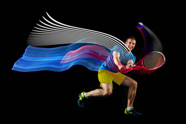Dynamic portrait of caucasian man playing tennis isolated on dark background with mixed colored stipes. Concept of sport, hobby, challenges, peace, politics - Fotoğraf, Görsel
