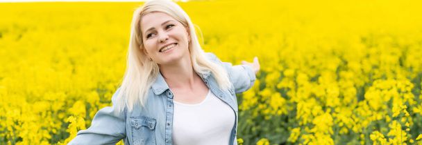 Portrait of attractive woman on blooming rapeseed field with sunset light. Yellow flowers and happy woman - Photo, Image