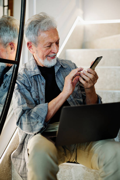 Um homem idoso sentado nas escadas e usando tecnologias. - Foto, Imagem