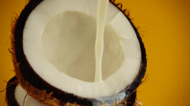 Splash of milk in a coconut on an orange background. Slow motion. - Felvétel, videó