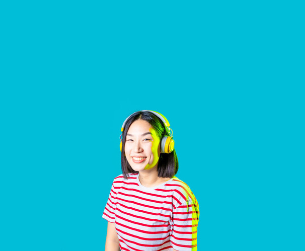 mujer asiática serena aislado en fondo azul escuchar música auriculares inalámbricos sonriente pancarta recortada - Foto, imagen