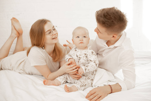 Glücklich freudig zufriedene Familie aus Frau, Mann und Säugling liegen weiße Tagesdecken. Gemeinsamer Familientag, Spiele mit Kindern - Foto, Bild