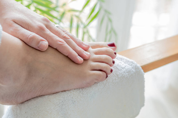 mãos de uma jovem mulher massageando os pés com unhas pintadas de vermelho depois de obter um pedicuro em casa - Foto, Imagem