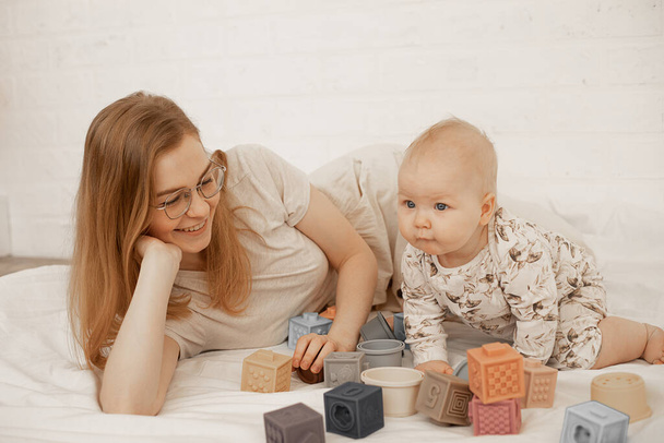 Mujer feliz, madre en gafas y niño jugando junto con juguetes en la alfombra de lino blanco en casa. Habilidades de actividad motora - Foto, imagen