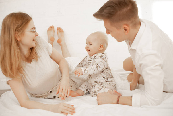 Happy joyful smiling satisfied family of woman, man and infant baby lying in white bedspread. Father day festive party - 写真・画像