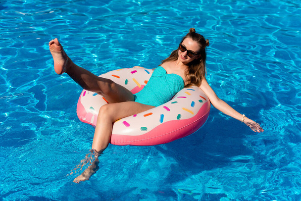 young woman in bikini swims on the inflatable water donut in the swimming pool - Foto, Imagem