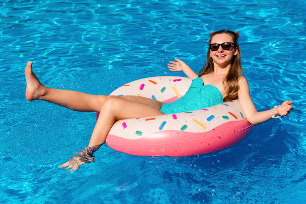 junge Frau im Bikini schwimmt auf dem aufblasbaren Wasser-Donut im Schwimmbad - Foto, Bild
