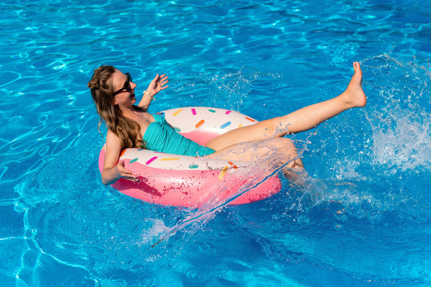 νεαρή γυναίκα με μπικίνι κολυμπάει στο φουσκωτό νερό ντόνατ στην πισίνα - Φωτογραφία, εικόνα