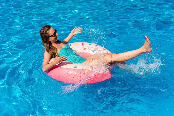 jonge vrouw in bikini zwemt op het opblaasbare water donut in het zwembad - Foto, afbeelding