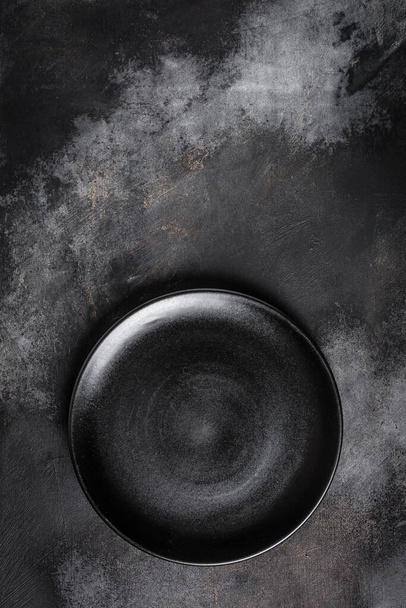 Black plate on textured black background. vertical image. top view. place for text. - Fotoğraf, Görsel