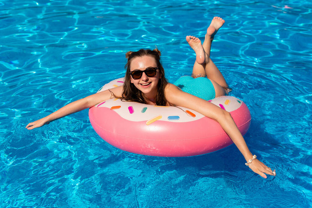 young woman in bikini swims on the inflatable water donut in the swimming pool - Photo, Image