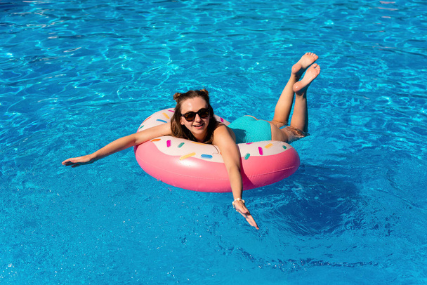 młoda kobieta w bikini pływa na nadmuchiwanym pączku wodnym w basenie - Zdjęcie, obraz