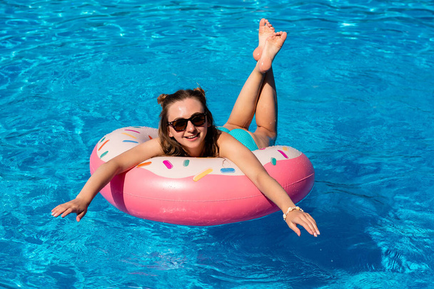 young woman in bikini swims on the inflatable water donut in the swimming pool - Fotoğraf, Görsel