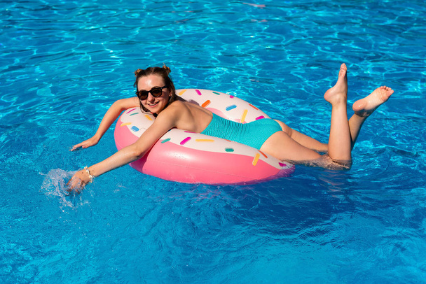Bikinili genç bir kadın havuzda şişme suda yüzüyor. - Fotoğraf, Görsel