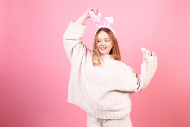 Una ragazza con le orecchie di coniglio balla su uno sfondo rosa. Vacanze pasquali, sorriso e festa. La ragazza sta posando nello studio - Foto, immagini