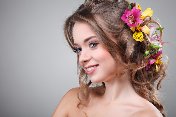 Beautiful  girl, isolated on a light - grey  background with varicoloured flowers  in hairs, emotions, cosmetics - Фото, зображення