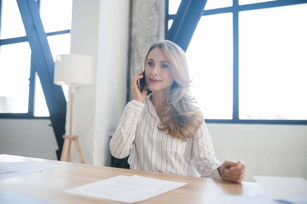 Una mujer de negocios rubia en su oficina hablando por teléfono - Foto, Imagen