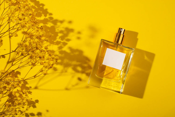 Transparante fles parfum met etiket op gele achtergrond. Parfumpresentatie met daglicht. Trending concept in natuurlijke materialen met prachtige plantenschaduwen. De essentie van vrouwen. - Foto, afbeelding