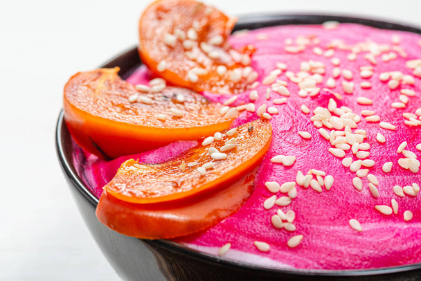 Close-up of slices of persimmon and sesame seeds on pink yogurt. - Fotoğraf, Görsel