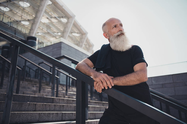 Photo of dreamy handsome man pensioner dressed black clothes looking far away enjoying cardio training outdoors city street - 写真・画像