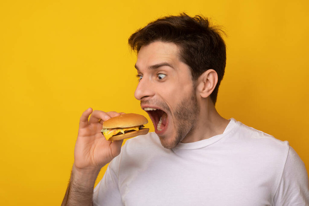drôle gars tenant hamburger mordant sandwich au studio - Photo, image