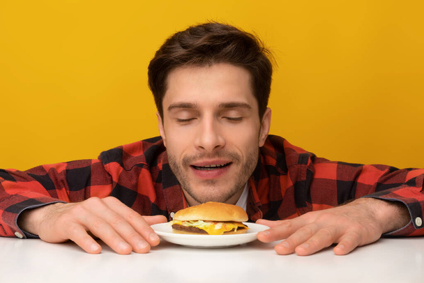 Primer plano de chico emocionado oliendo sabrosa hamburguesa en el estudio - Foto, imagen