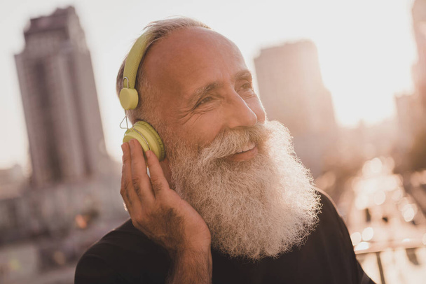 Photo of cheerful old man listen audio song music rest training break wear earphones t-shirt urban town outdoors - Foto, Bild