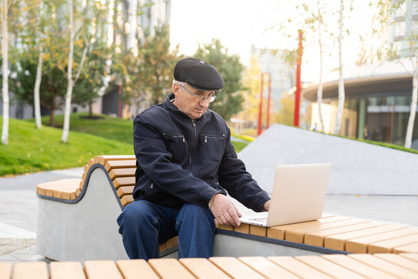 Les personnes âgées utilisent un ordinateur portable dans le parc. Beau senior en lunettes de travail à l'extérieur. - Photo, image