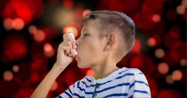 Caucasian boy using a asthma inhaler against red spots of light on black background. medical and healthcare concept - Foto, imagen