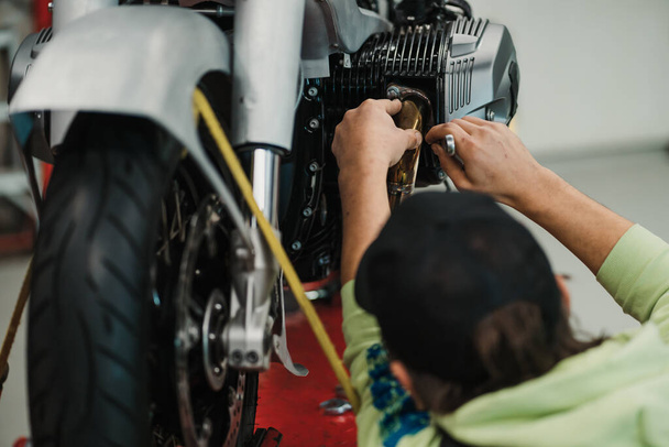 Man fixing a motorcycle in a modern workshop - Фото, изображение