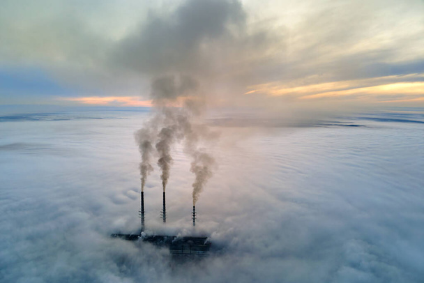 Uitzicht vanuit de lucht op hoge pijpen van kolencentrales met zwarte rook die bij zonsondergang de vervuilende atmosfeer opgaat - Foto, afbeelding